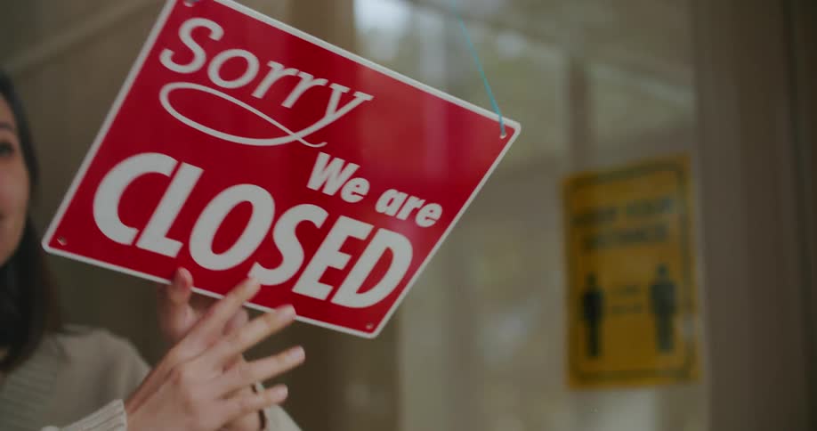 A woman goes to the window and changes the open sign to closed