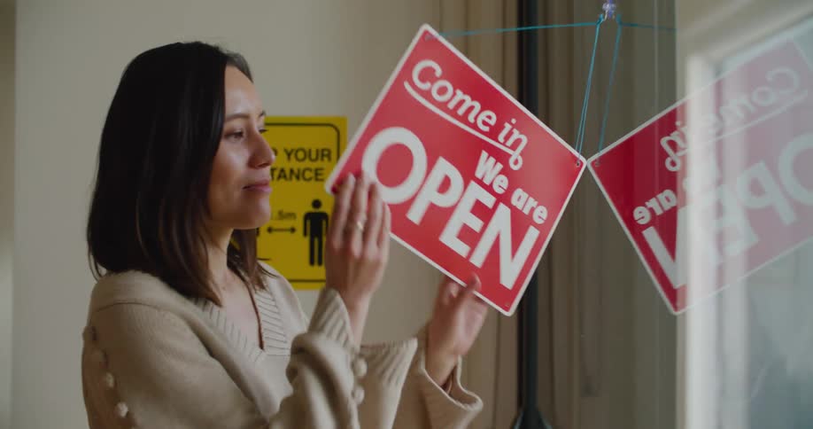 A woman looks around outside through the window before flipping the sign to closed