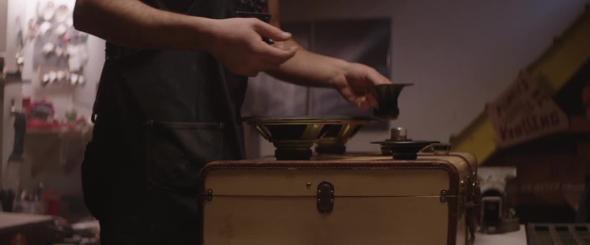 A man picks up a speaker and places it on a suitcase