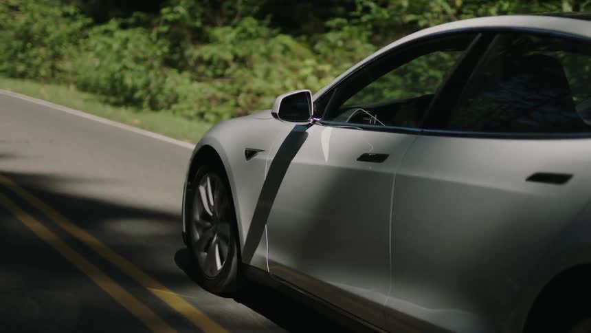 A white car drives on a tree and bush-lined road