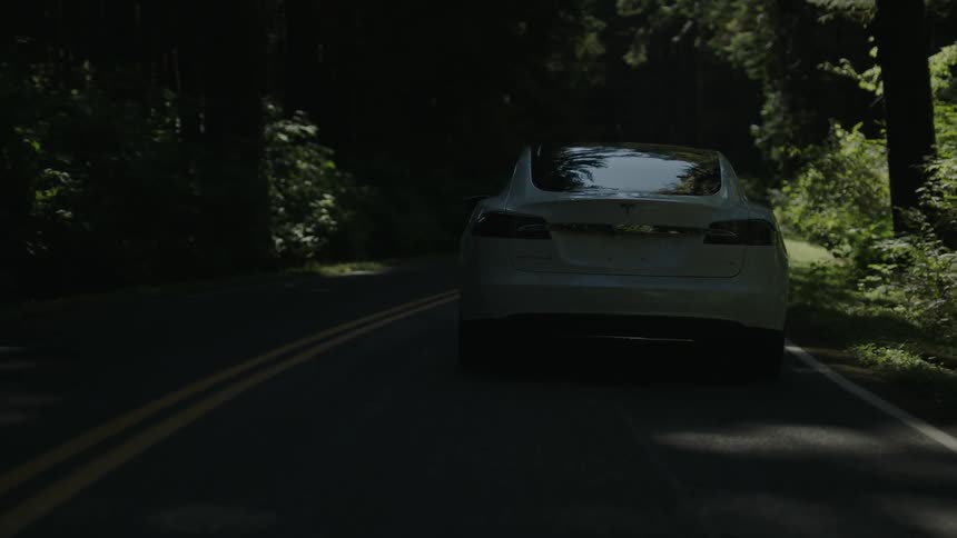 A white car drives down a shadowed road