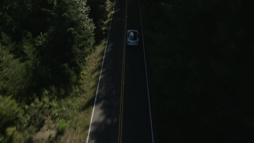 A car is traveling down a road surrounded by woods
