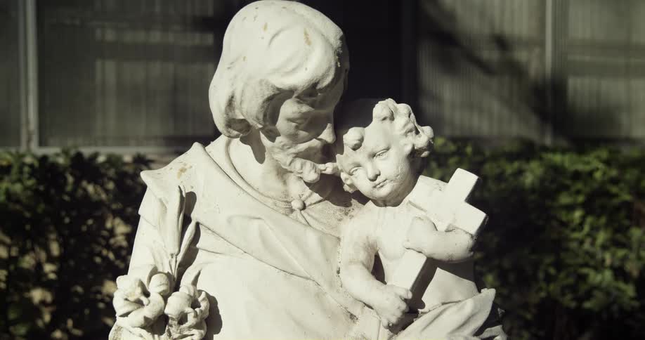 A sculpture of a man holding a child clutching a cross in a sunny garden