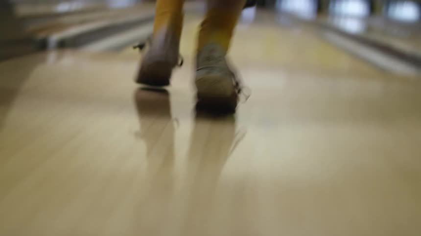A woman in a bowling alley throws a ball down the lane towards the pins