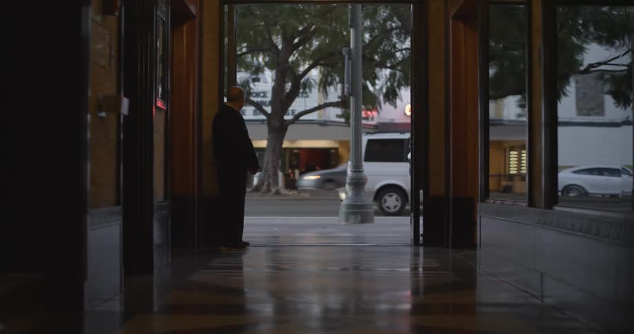 Bald man in suit watches the street with vehicles passing by