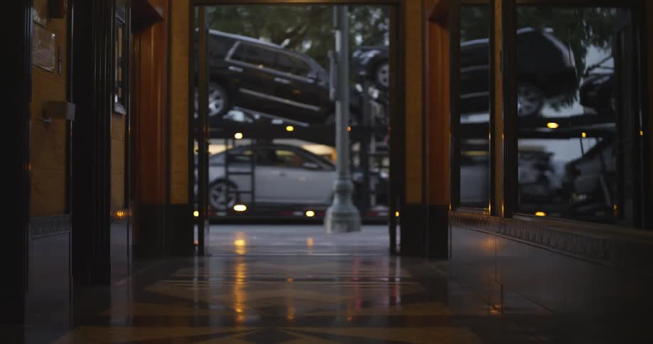 A buildings window reflects a semi carrying new vehicles while driving down a city street