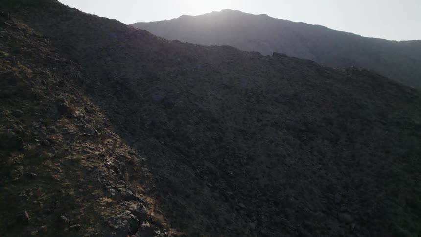 Plant covered mountain range under a bright sun on a clear day