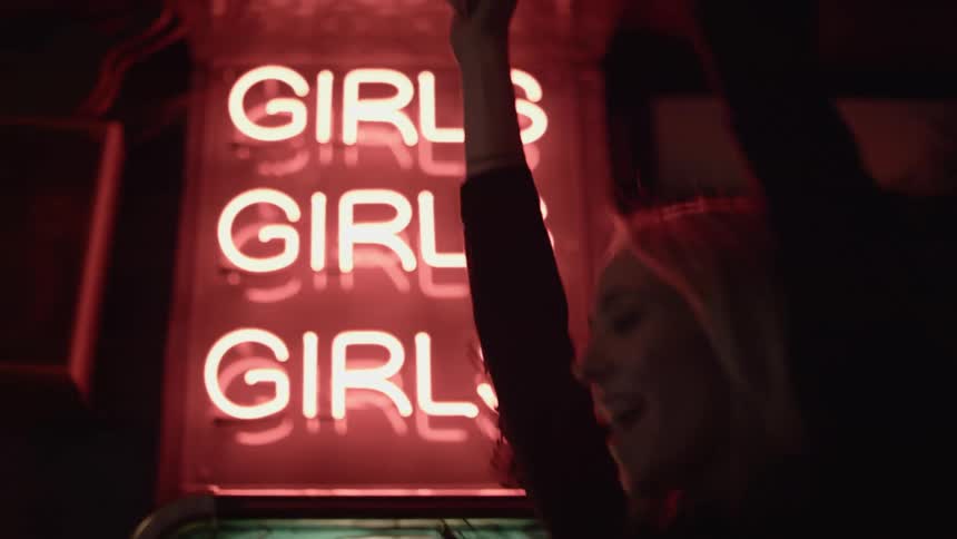 Young blonde woman dancing in front of a neon sign on the city street at night