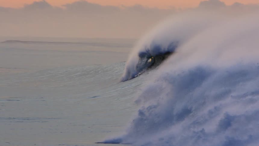 Ocean waves splashing as they roll in under an orange sky