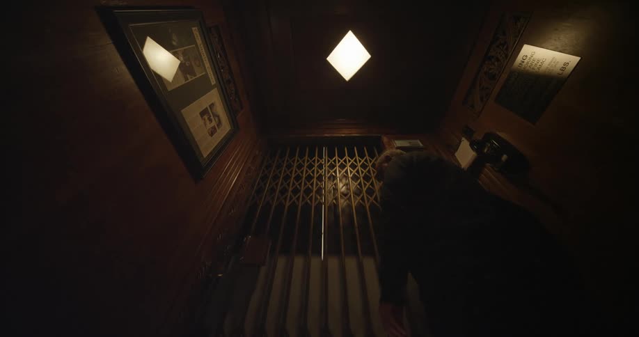 Elderly man closes the door on a vintage dimly lit elevator before going up