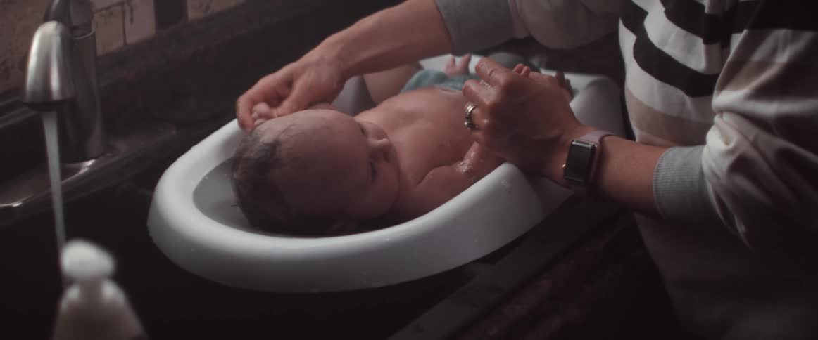 Woman with sweatshirt and smart watch washes baby in tub