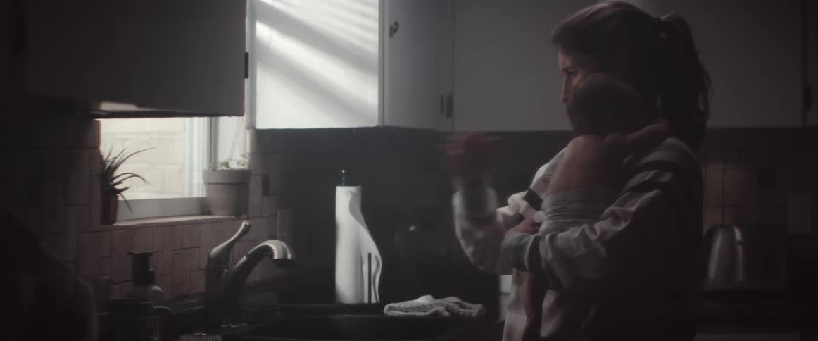 A woman in a kitchen holding a baby and opens a water faucet