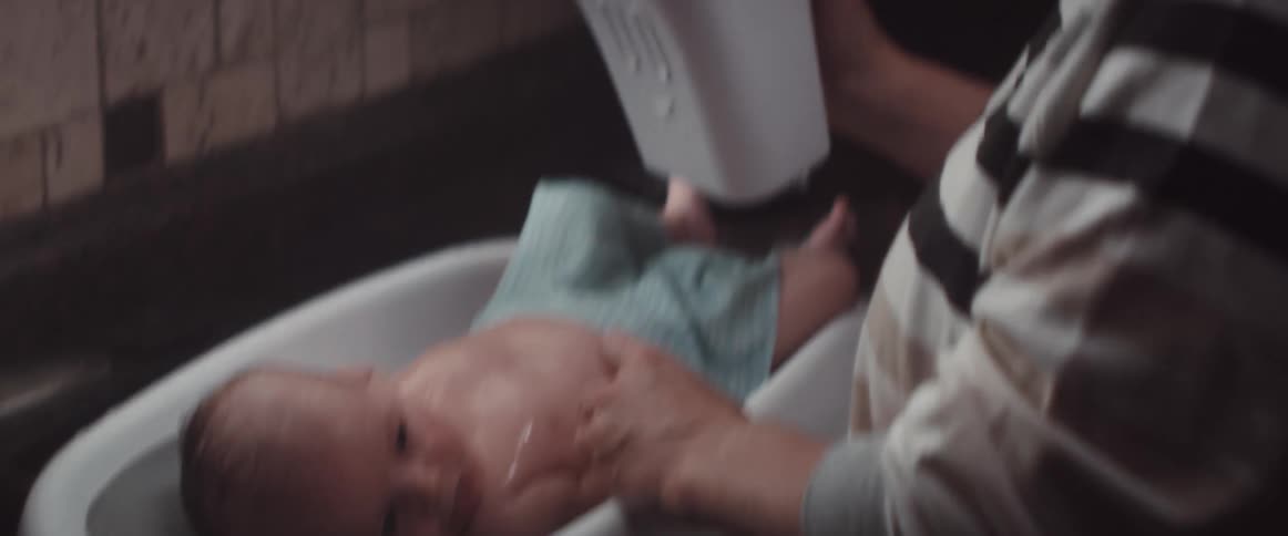 Mother bathing his son on a small baby portable bathtub on the kitchen