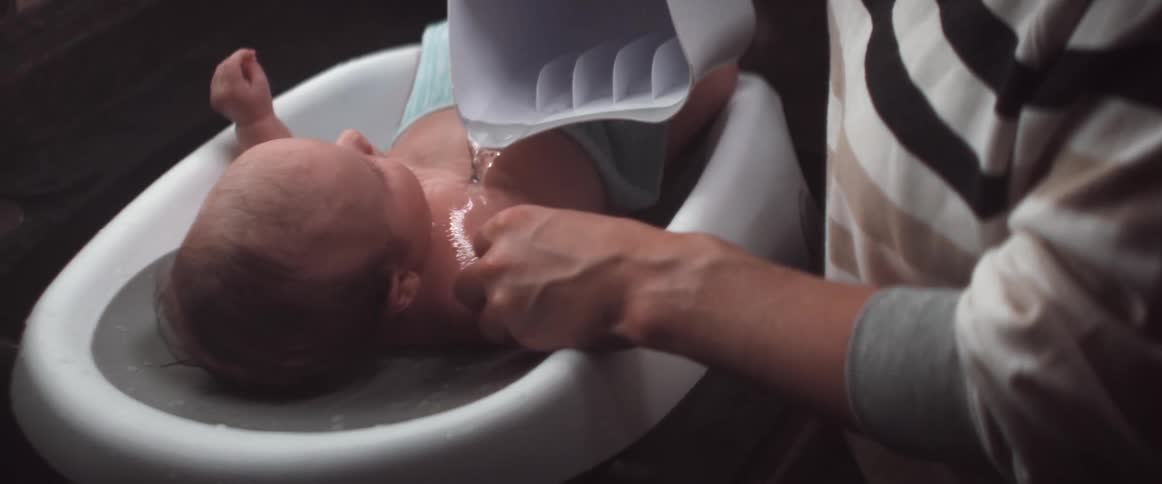 A man gives his baby a bath in the sink using a pitcher and plastic tub
