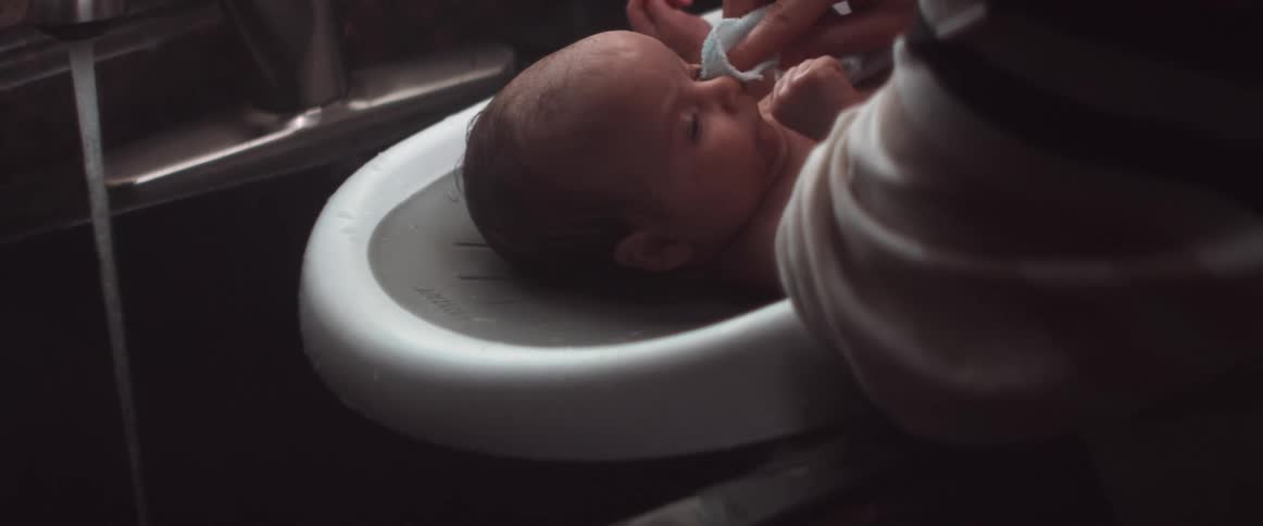 A woman is gently wiping the face of an infant laying in a baby bathtub