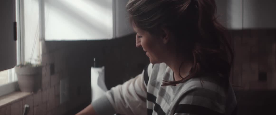 A woman in a kitchen with a wall window and potted plant in the background