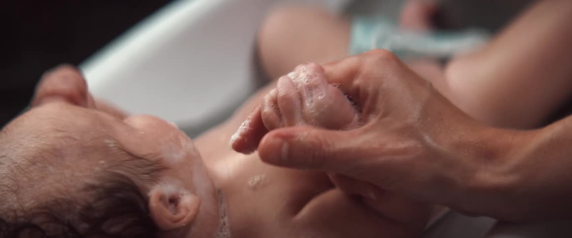 Mother giving her son a bath on a small portable baby bathtub at home