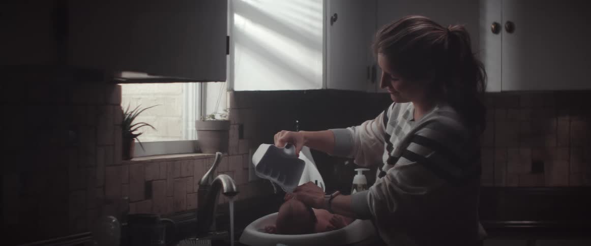 Mother bathing her son on a small baby portable bathtub over the kitchen sink