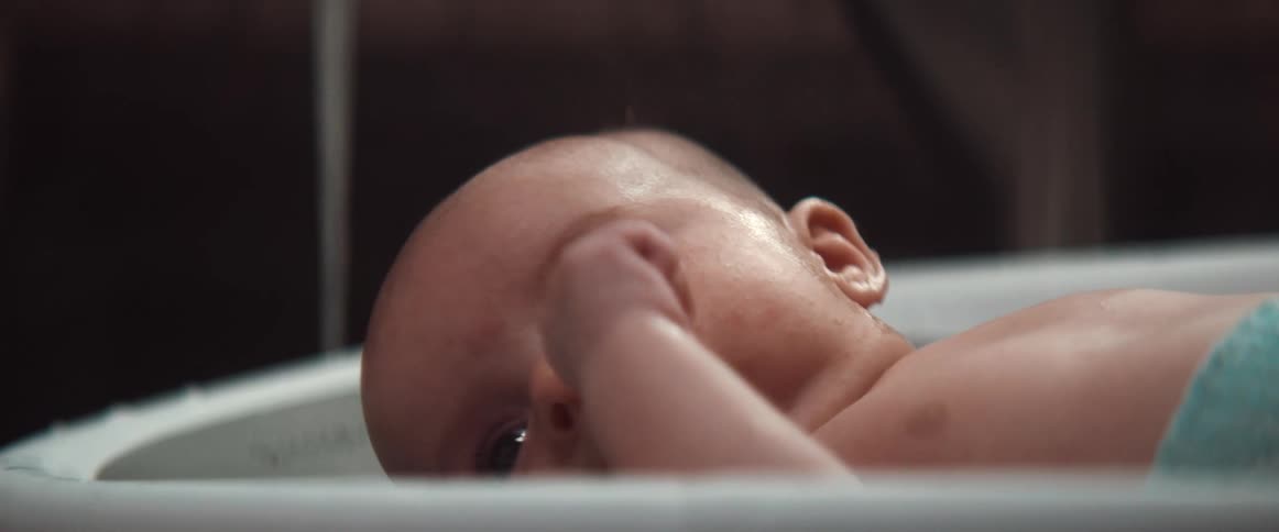 Baby lies in shallow bathing platform as water runs in background