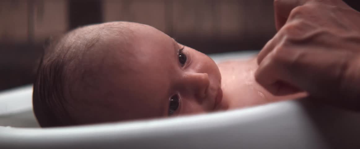 Mother gives her son a bath on a portable baby bathtub