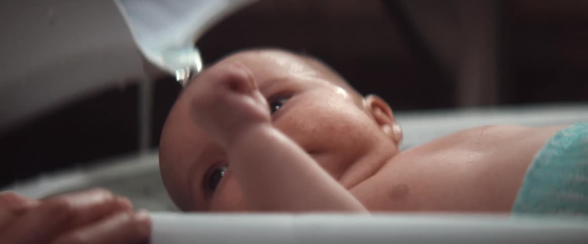 Woman gives baby bath in tub