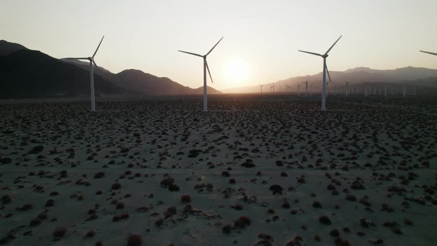A landscape with wind turbines with a mountain range the sky and clouds in the background