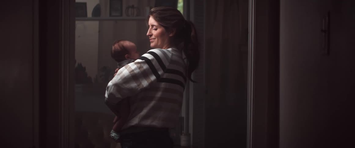 A woman in a room holding a baby with a wall and a light switch