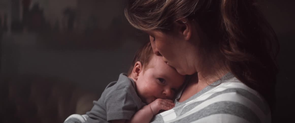 A woman in a room holding a baby with a couch and a wall in the background