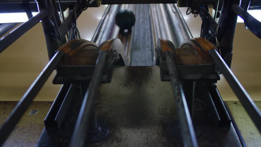 Green bowling ball rolling on the rails back to the bowling lane