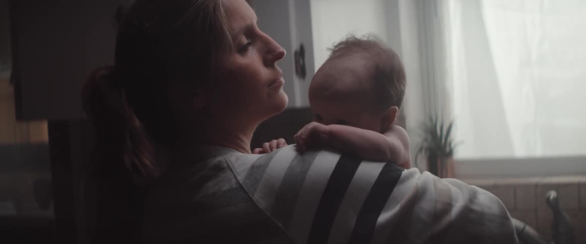 Mother with ponytail and sweatshirt holds baby caressing and giving him a kiss in the kitchen