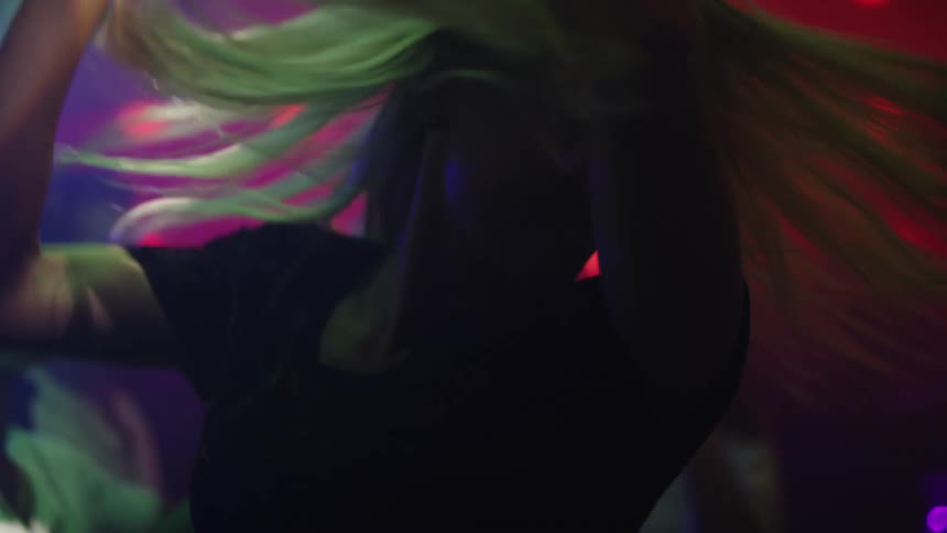 Blonde woman with black sweater dances with people in bar