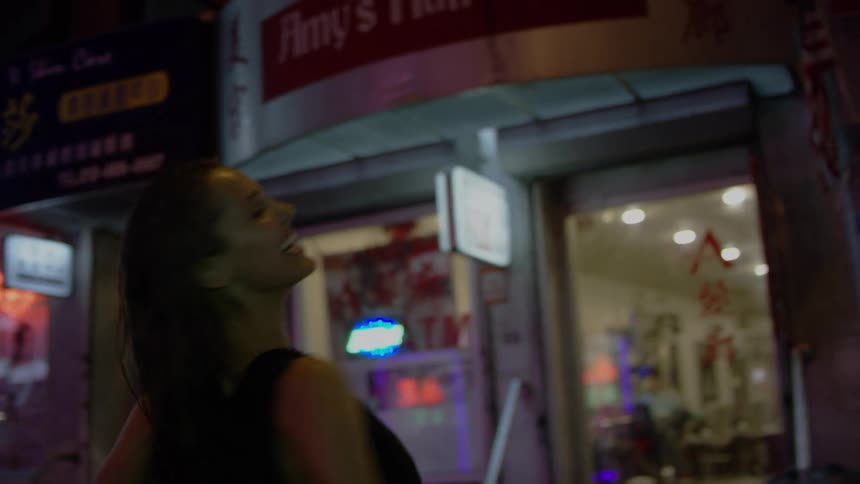 Woman spins laughing and smiling standing on street between storefronts in city at night