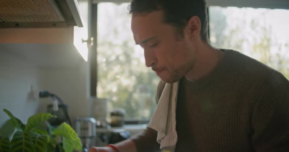 Man wearing sweater stirs and tastes meal simmering in pan on stove