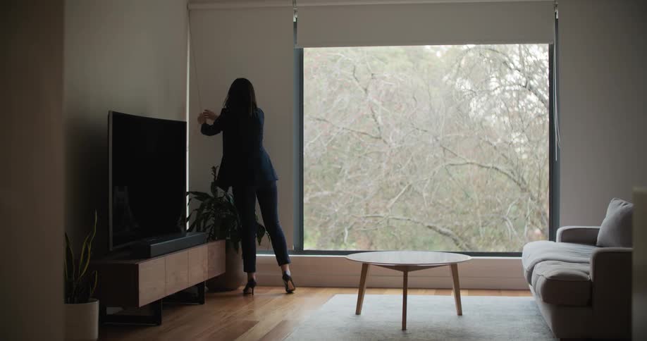 Woman in black suit and high heels opens window shade in living room