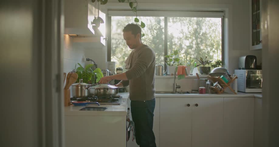 Young man cooking dinner in the kitchen at home at sunset