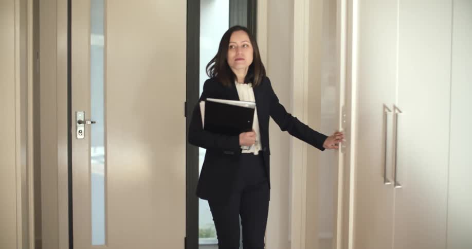 A woman walks through her front door and sets her binder on a counter before making a call on her phone