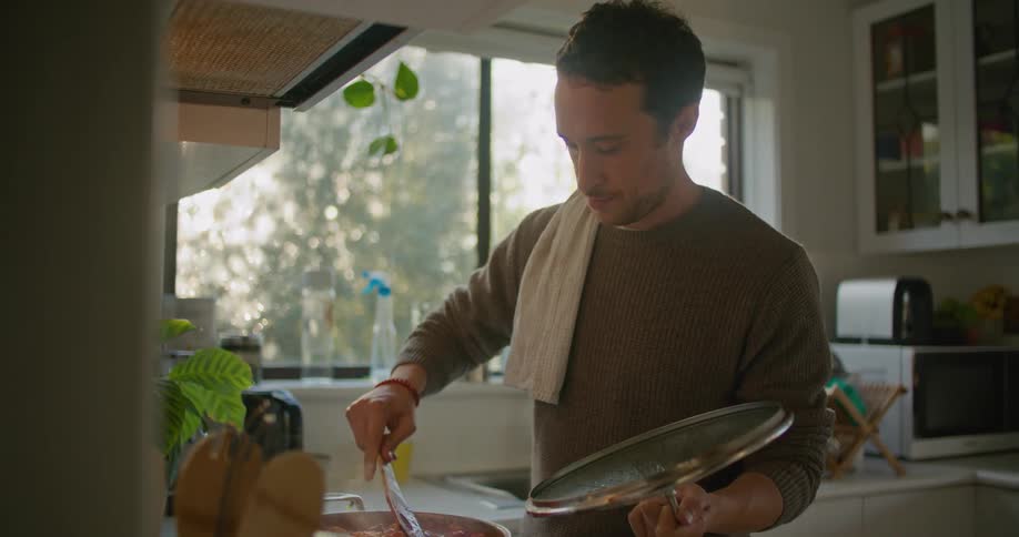 A man in a kitchen using a smart phone while cooking a sauce in a pot