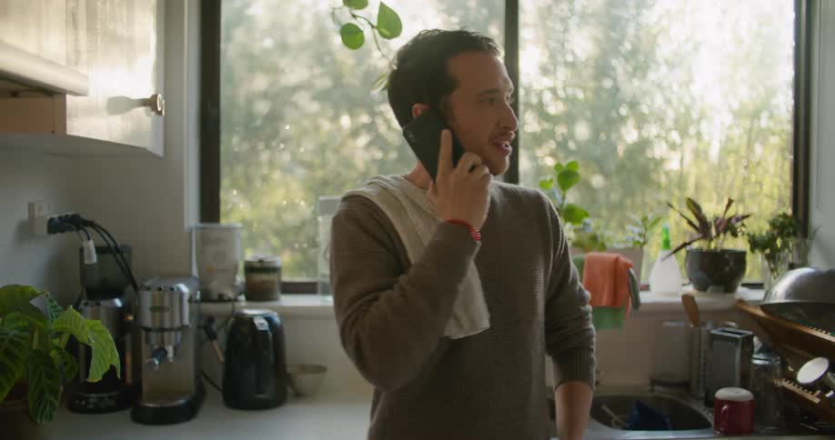 A man is talking on a cellphone while cooking a meal indoors during the day