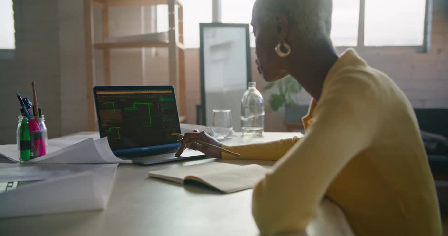 A woman works on a laptop and notebooks on a large table in an office