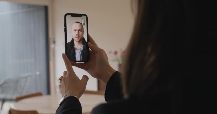 A woman talks to a man via video chat on a smart phone in an apartment