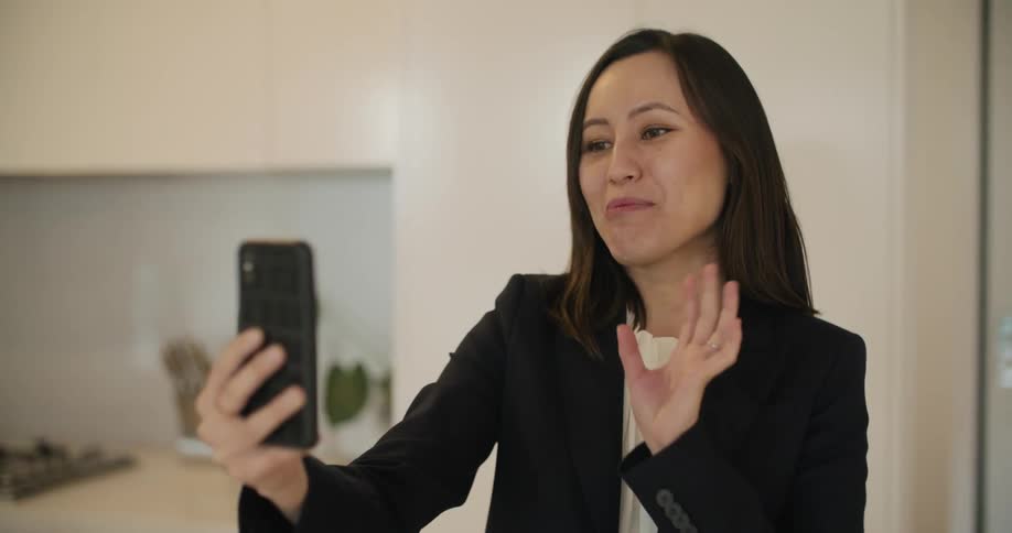 Young woman wearing business clothes greets someone on a video call in her smartphone