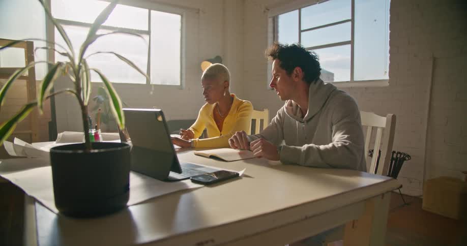 Coworkers sitting at a desk in the office working on laptops at morning