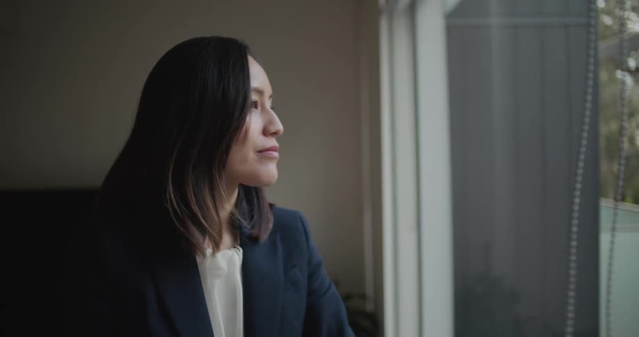 A woman gives a slight smile as she opens the blinds in a window