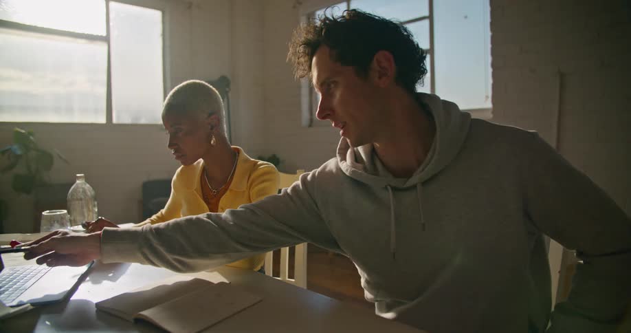 Woman with yellow sweater and man wearing gray hoodie work on laptop in the office