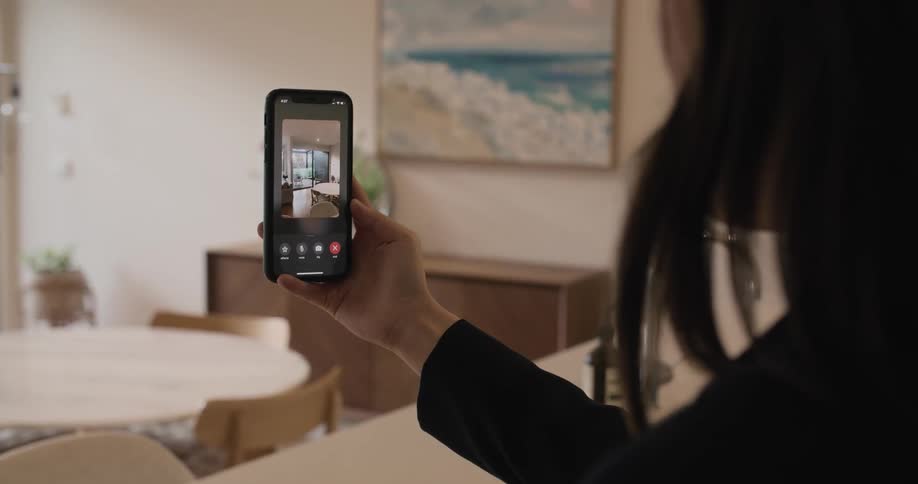 A woman is holding a phone up taking video in a kitchen