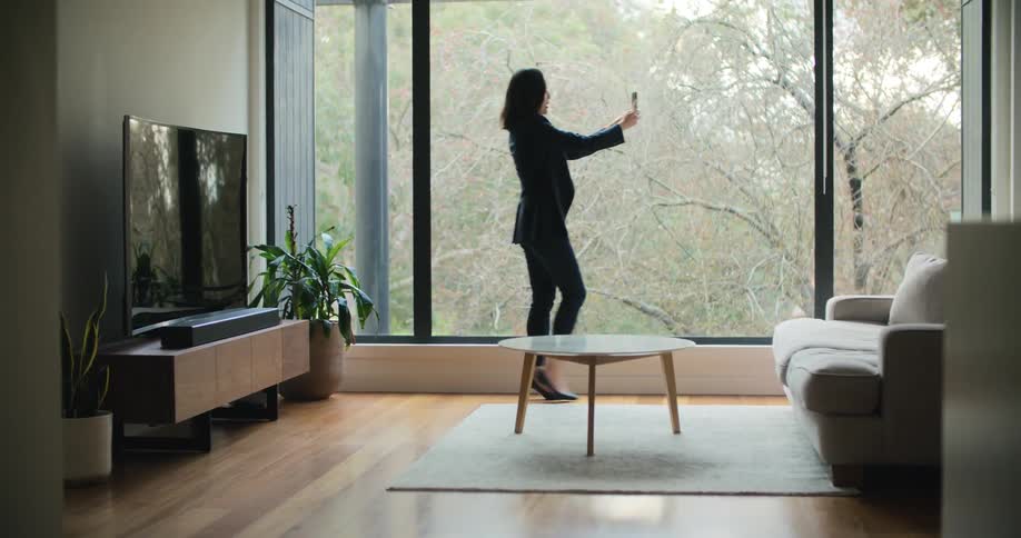 A woman walks around a living room holding her phone up taking a video