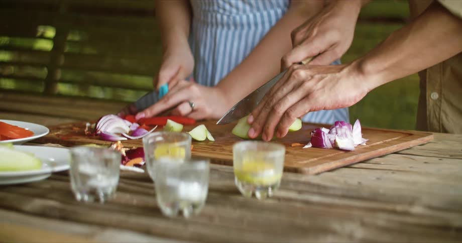 A woman and man are chopping vegetables with knives on a cutting board