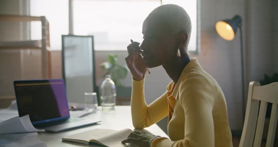 Woman sitting at a desk in the office talking while working on a laptop