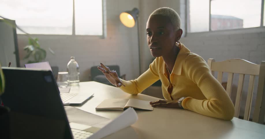 Woman working in office has video meeting via one computer while taking notes and referencing laptop