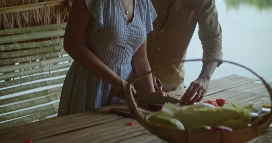 A man showing a woman how to cut vegetables with a knife